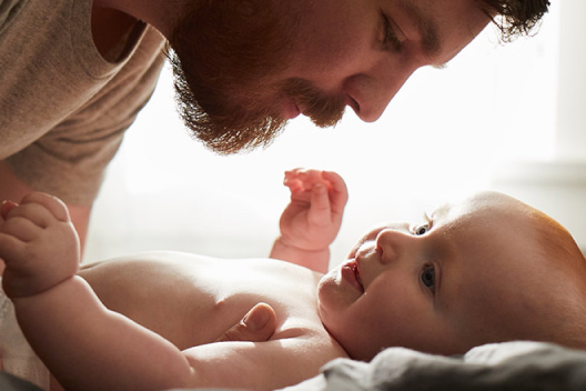 A father prepares to pick his smiling baby up off of a blanket